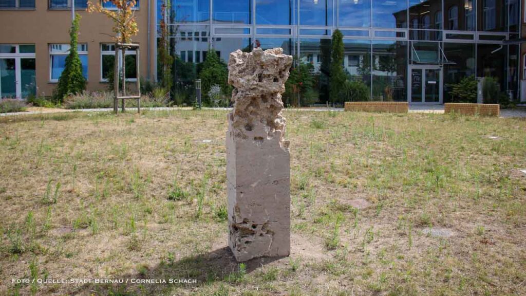 Ein Blick ins Innere der Zeit: „Terra Exalta“ auf dem Kulturhof Wer den Kulturhof an der Breitscheidstraße 43 besucht, stößt auf ein Werk der Berliner Künstlerin Birgit Cauer. Für „Terra Exalta – Leben zwischen Himmel und Erde“ wählte sie Travertin, einen offenporigen Kalksteinblock. Mit Hammer, Meißel und Bohrer arbeitete sich die Künstlerin tief in den Stein vor. Durch geschaffene Nischen und Hohlräume gibt sie den Blick frei auf urzeitliche, Millionen Jahre alte organische Einschlüsse – ein Werk, das zum genauen Hinsehen und Entdecken einlädt.
